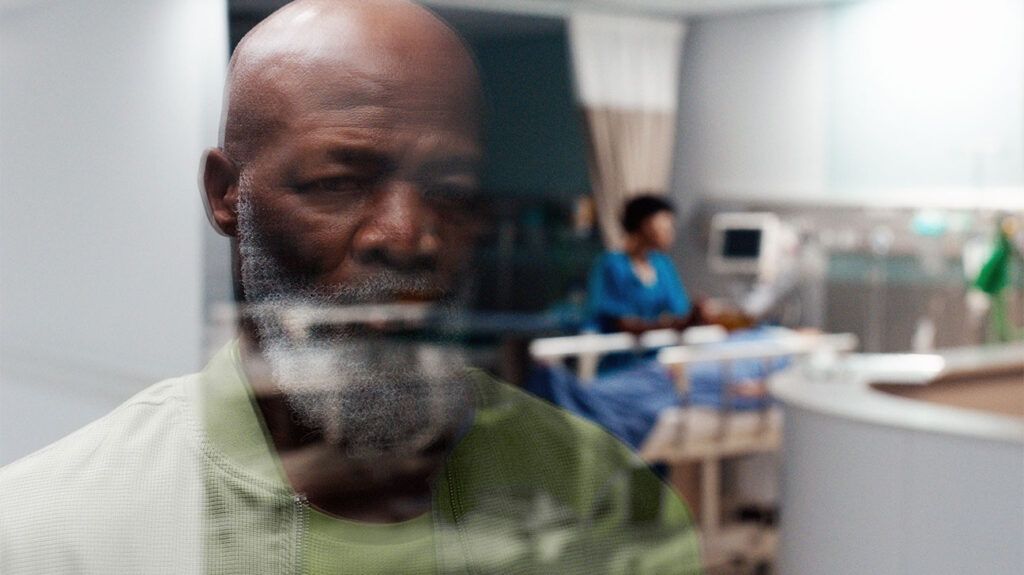 An elderly man, a nurse and a patient being reflected on a window at a hospital