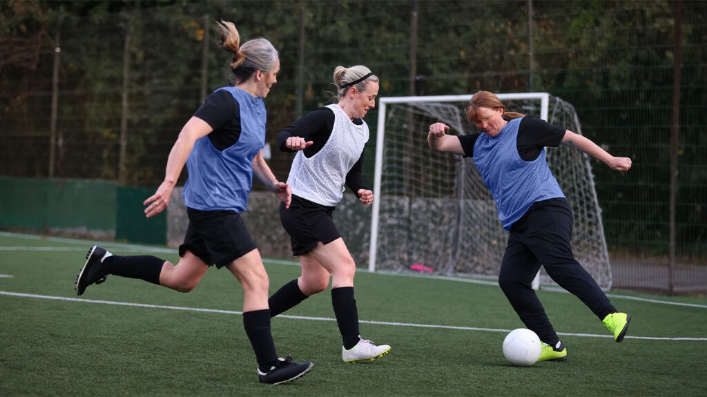 Three women playing soccer on a field