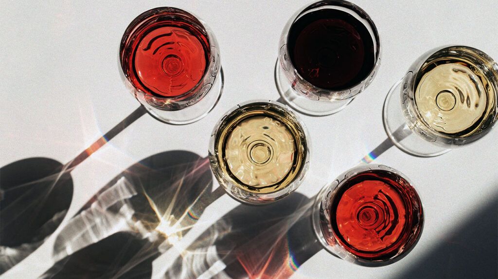 five glasses of wine, one of red wine, two of rose, and two of white wine, photographed from above