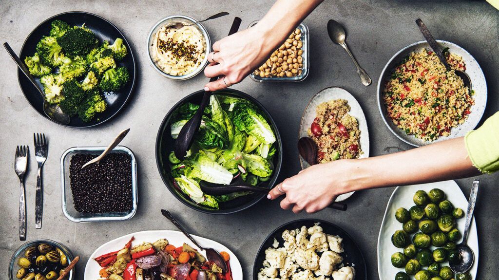 Various healthy Mediterranean-inspired dishes in plates on a table and a person mixing a bowl of fresh salad