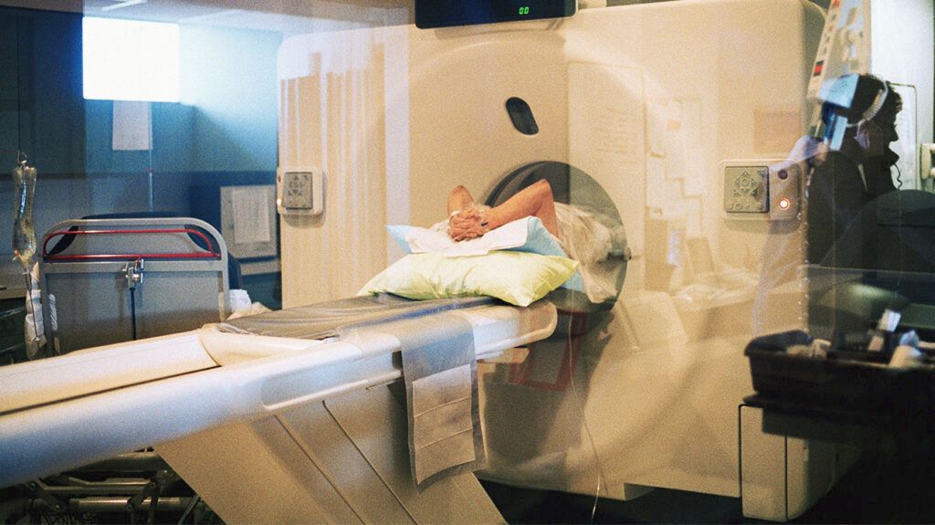 A patient getting a CT scan as they clasp their hands over their head