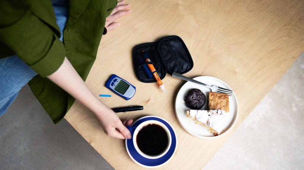 Photo of a blood glucose meter next to a cup of coffee and a plate of sweets