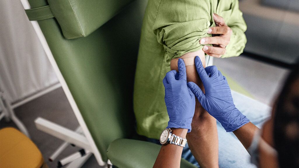 Healthcare professional putting a band aid on a person's arm after drawing their blood