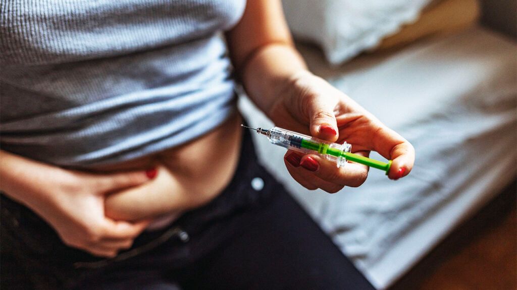 Woman giving herself an injection into  the abdomen injection site.