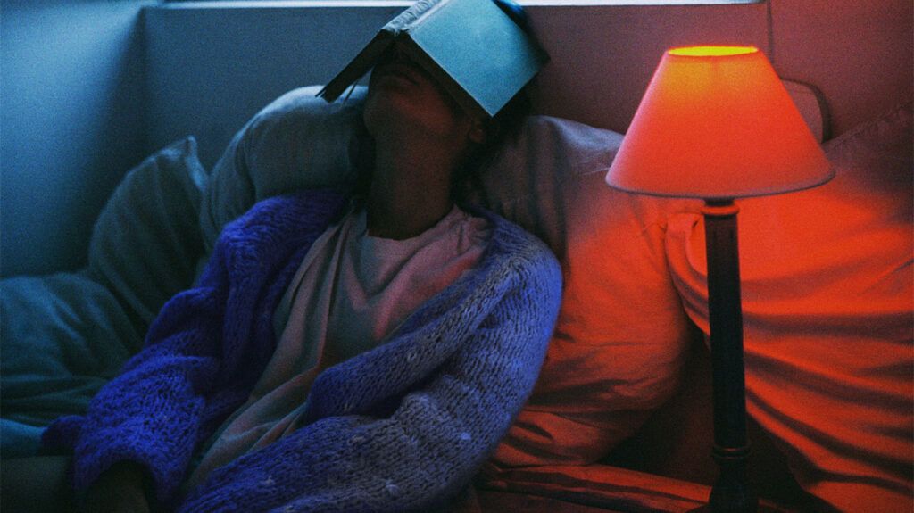 person reclining in bed with a book open on their face