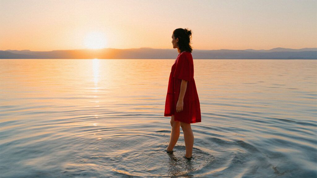 A woman looks out into the sunset as she stand in a body of water