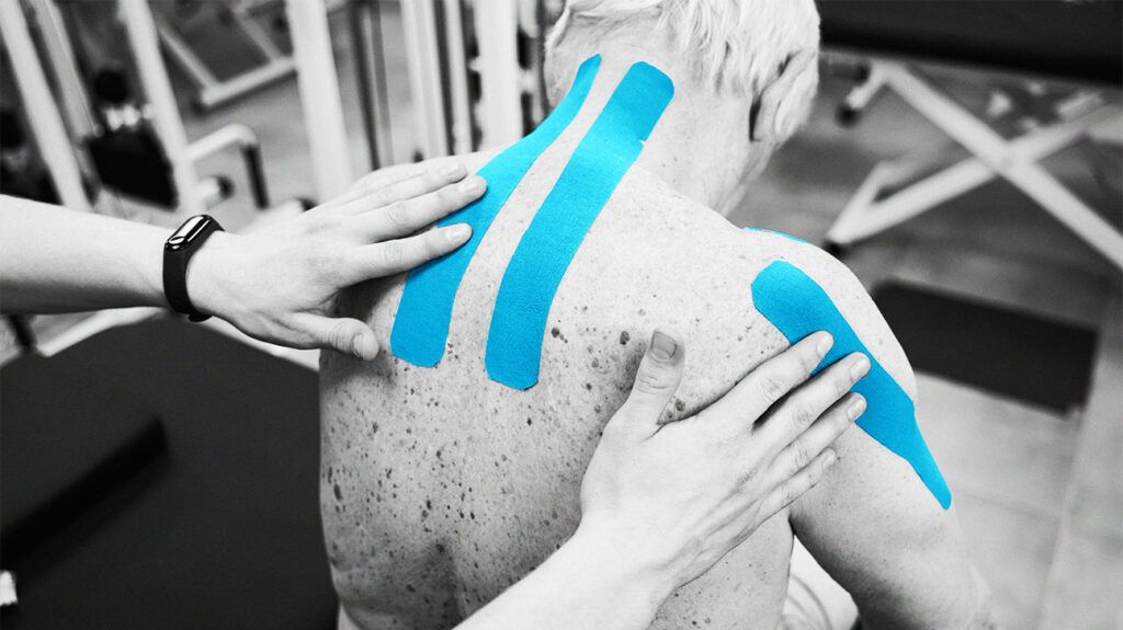 A physical therapist applying blue tape to a man's back as part of rehabilitation after psoriatic arthritis surgery.