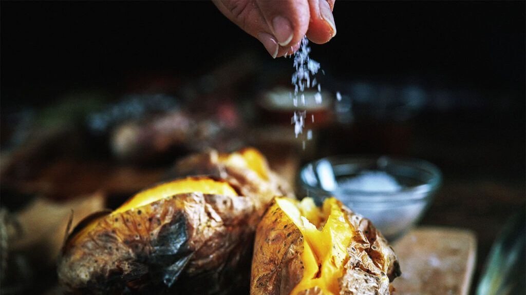 A person salting baked potatoes