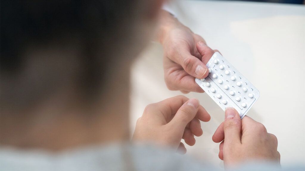 A gynecologist handing a person a tray of contraceptive pills.