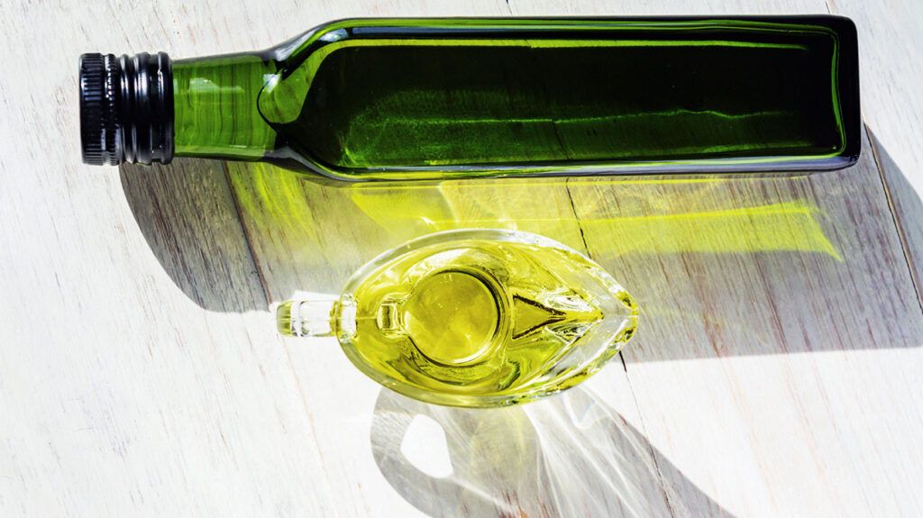 glass sauceboat with extra virgin olive oil and green bottle on wooden table-1