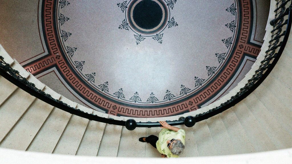 An older adult woman going up a spiral staircase