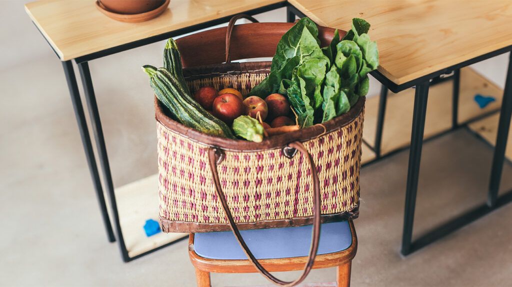 A woven bag full of fruits and vegetables on a chair