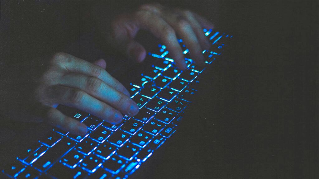 Closeup of a person typing on a backlit keyboard.