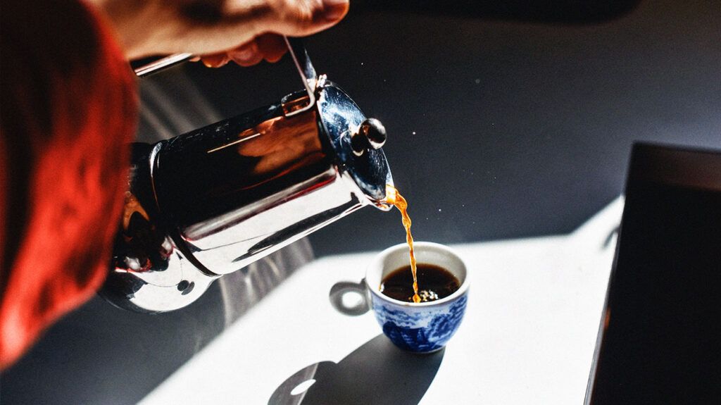 A moka pot pouring coffee into a cup 1