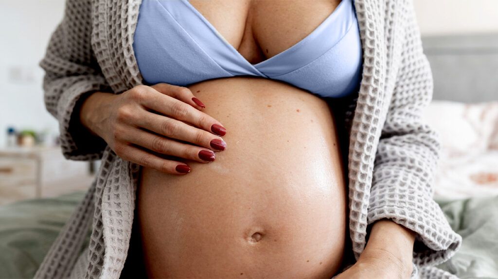 Closeup of a pregnant person with a hand on their stomach.