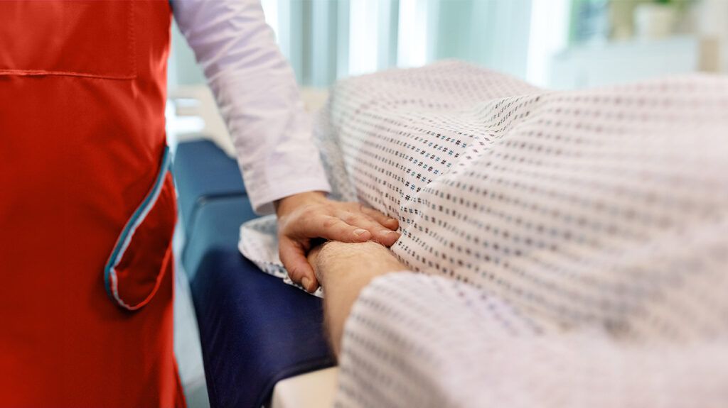 A healthcare professional holds the hand of a patient to comfort them while they are treated at hospital