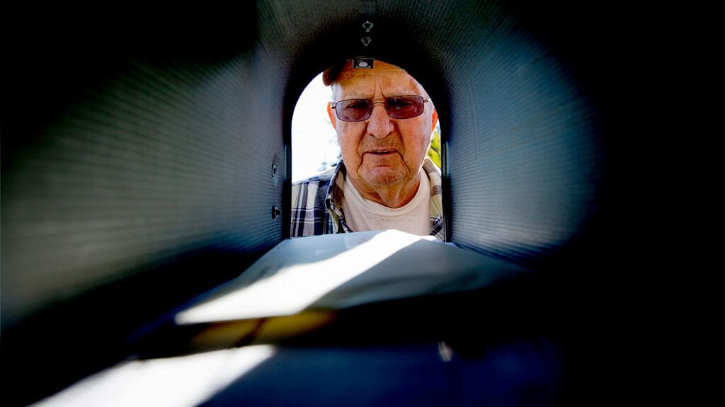 An older adult is looking in a mailbox.