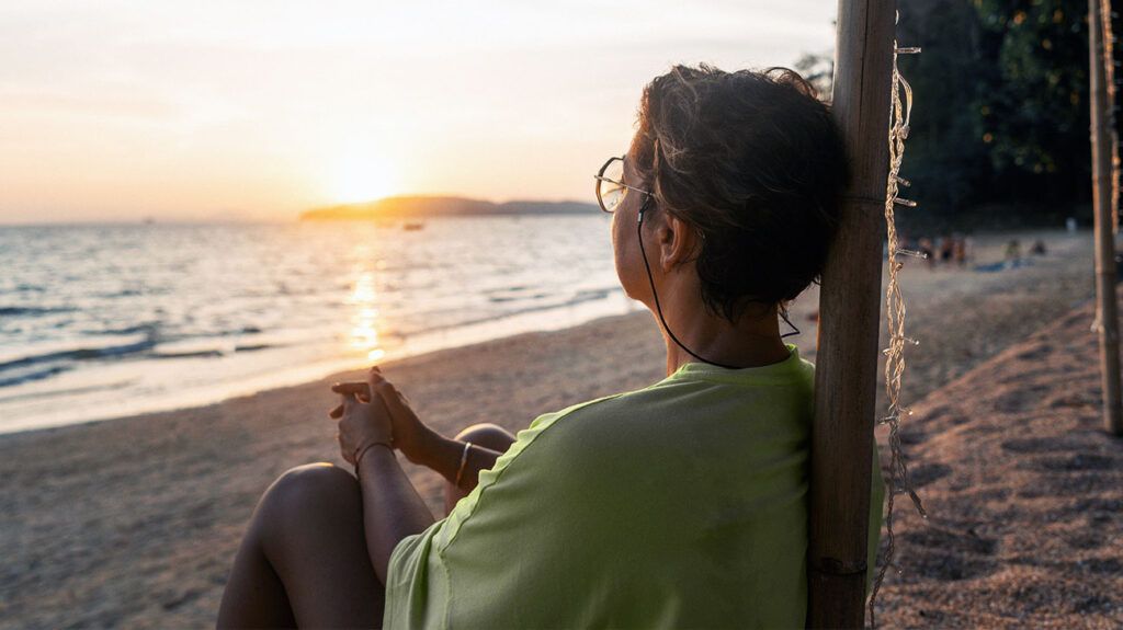 An older adult female sitting on the seashore looking into the sunset