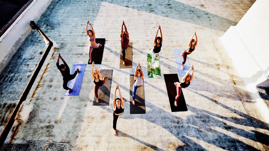 An overhead view of nine people in the warrior pose during a yoga class on a rooftop