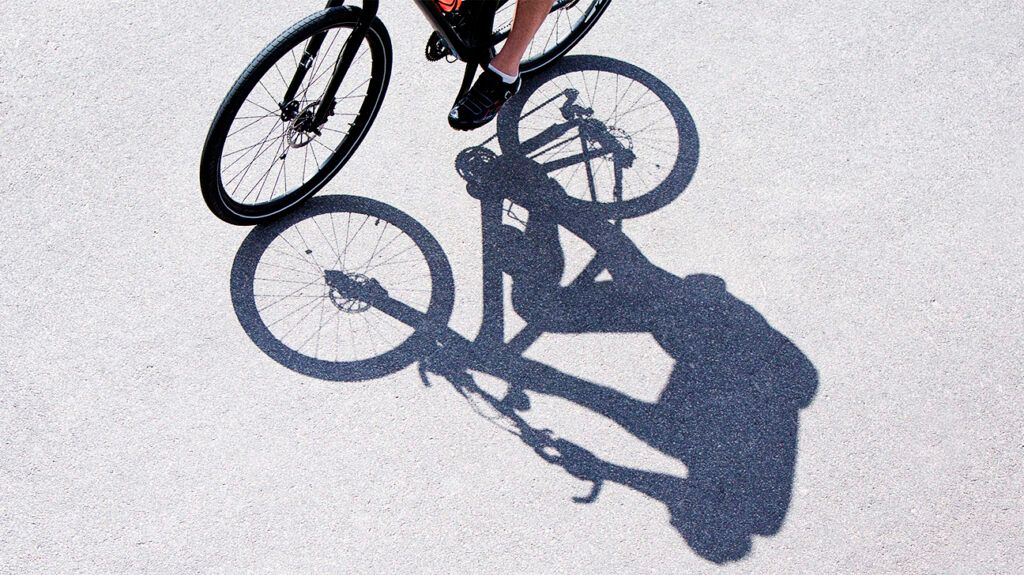 Man riding bicycle with his shadow showing on the ground.