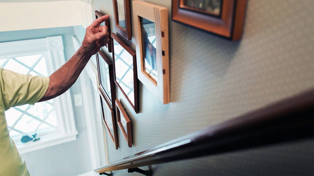 older person's hand pointing at framed pictures on wall