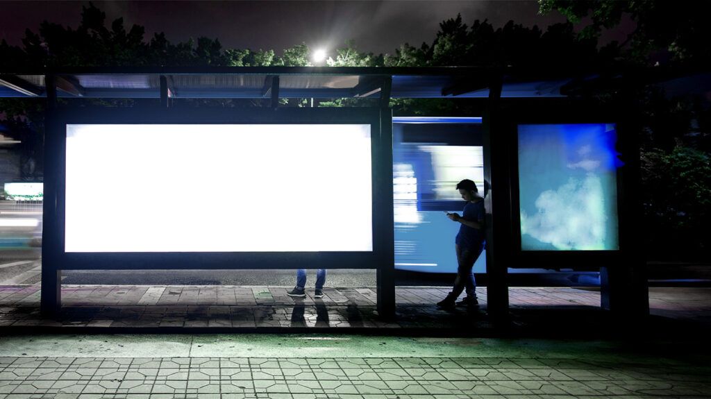 A man waiting at a bus stop at nighttime.