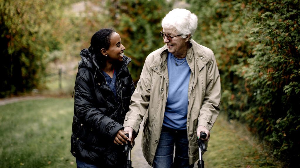 A person assists an older adult while walking