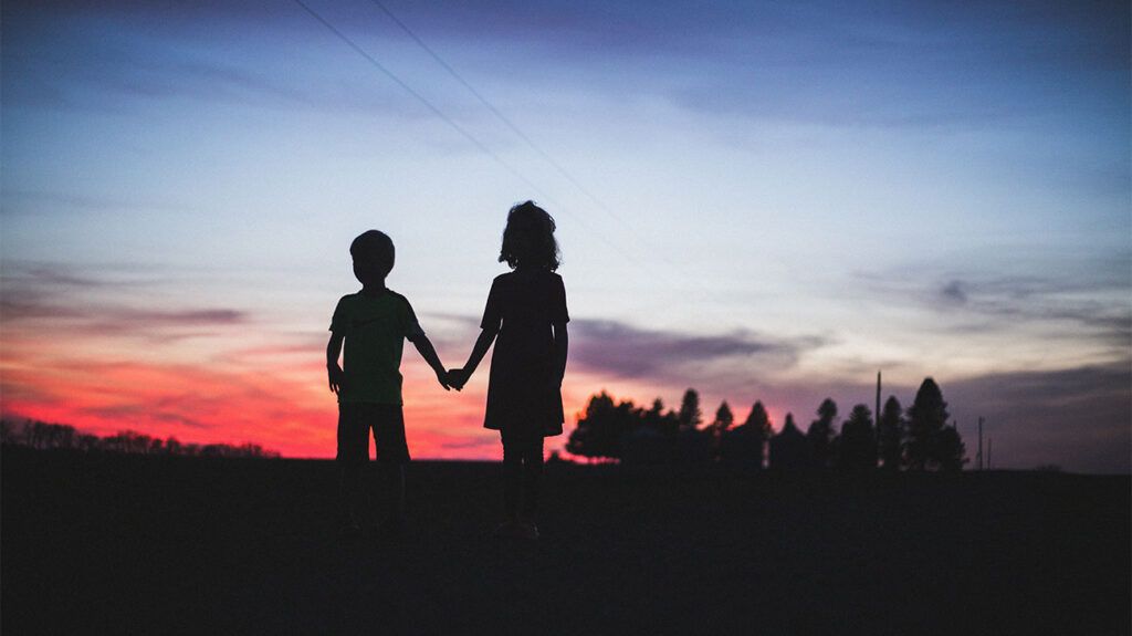 silhouettes de deux enfants contre le ciel au crépuscule