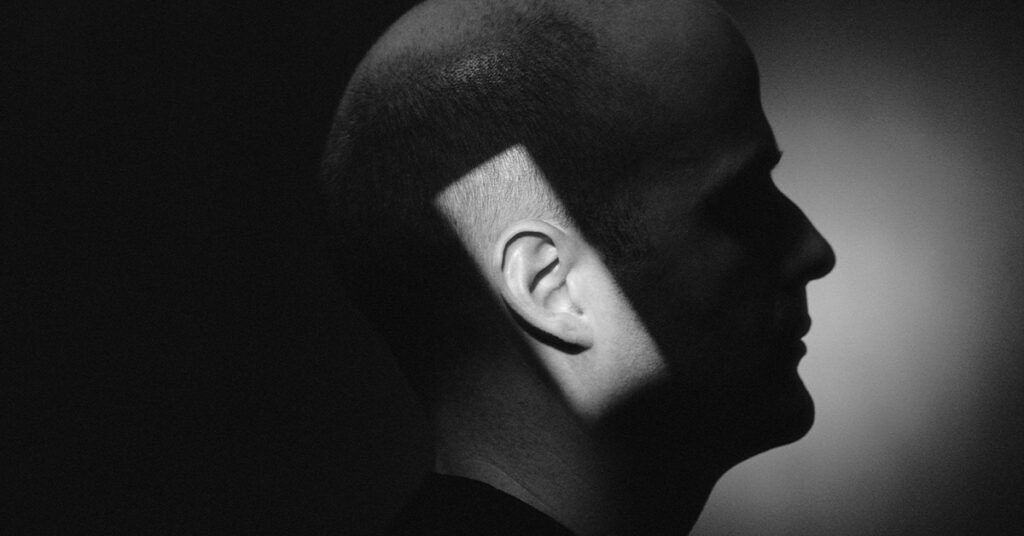 A rectangle of light shining on a man&rsquo;s ear. The rest of his face is in shadow.