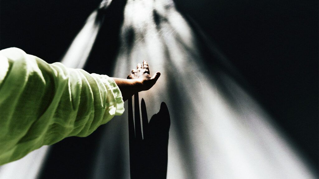 A hand reaches out to the light from above against a wall