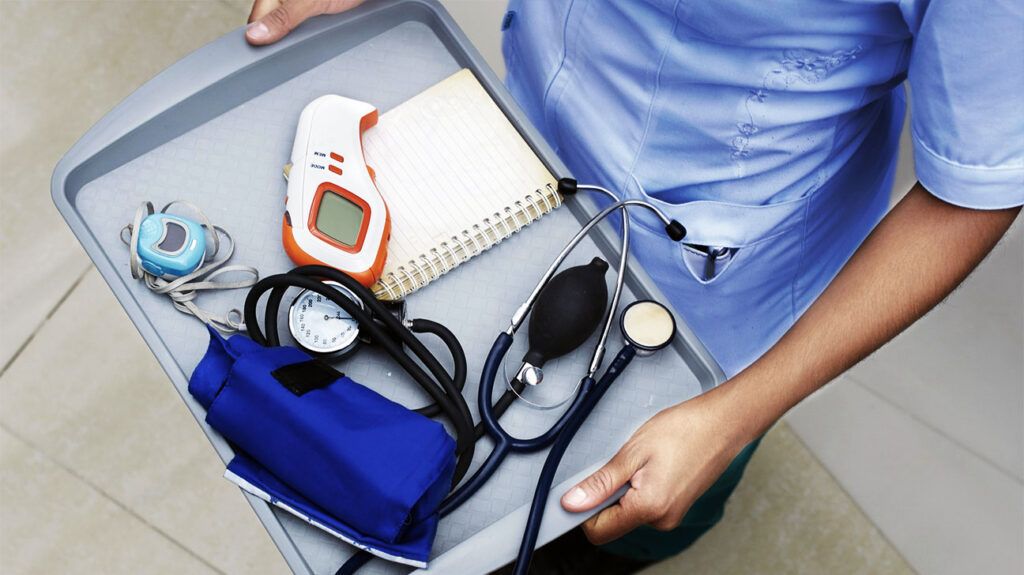 A nurse holding a tray of blood pressure monitoring equipment.