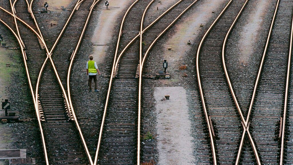 Zoomed out shot of rail tracks with a railroad worker standing in between the lines wearing a high-visibilty jacket
