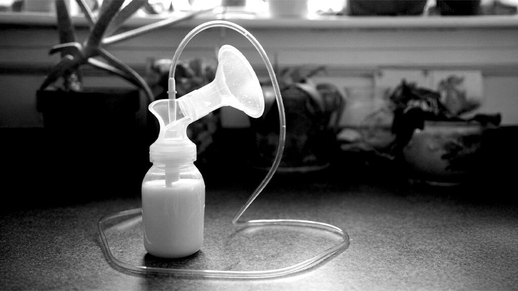 A breast pump sitting on a wooden table with the attached bottle full of milk