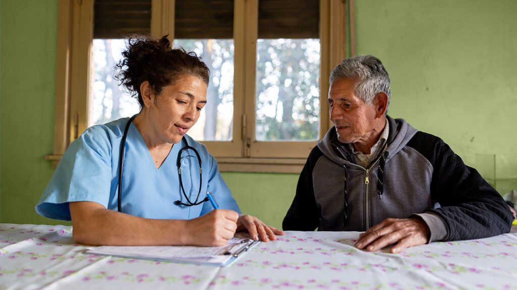 a female doctor in a blue coat is talking to an elderly patient in a gray hoodie