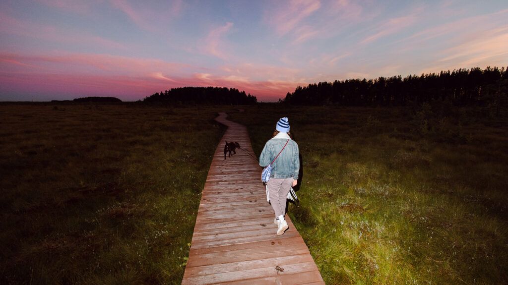 A person walks a dog on a trail outdoor at sunset