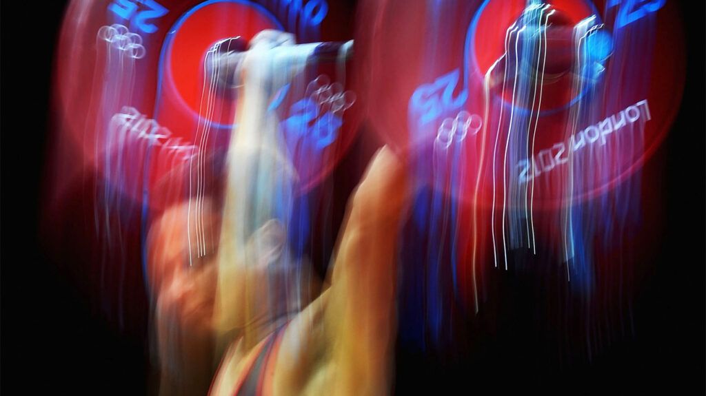 A blurry image of a weightlifter lifting a barbell above his head