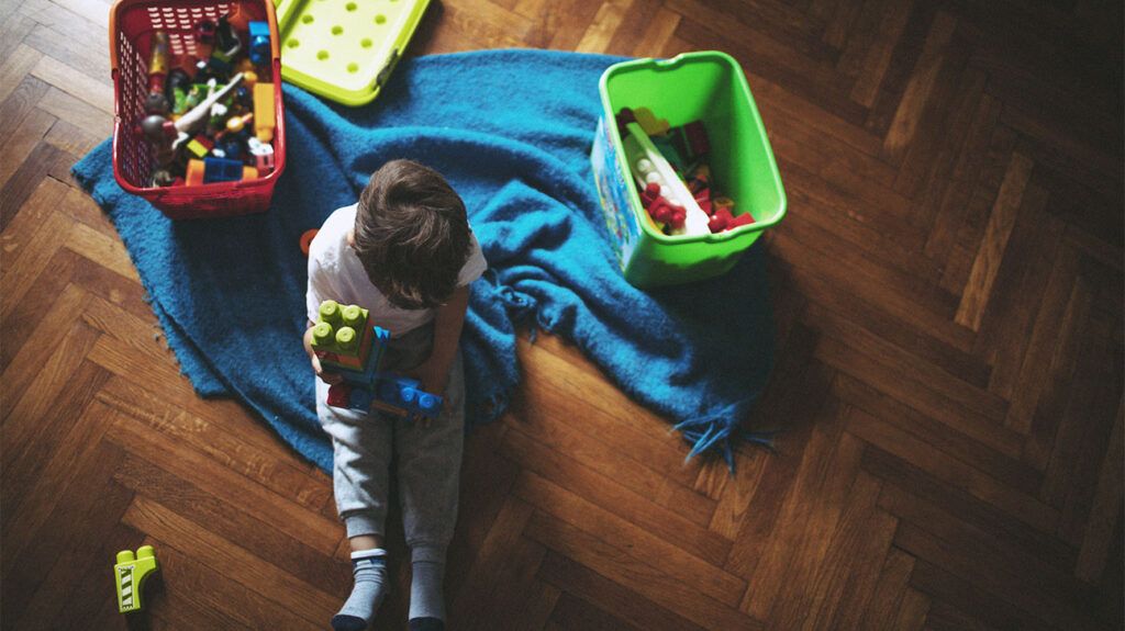 A child playing next to a blue blanket and a green storage tub.-2