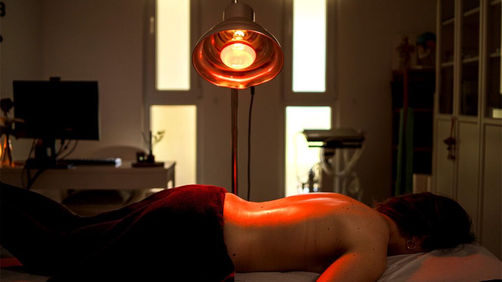 A person lying shirtless on their front with a red light shining above them.-1