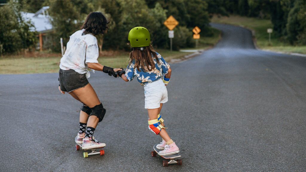 Adult holding hands with a child while skateboarding