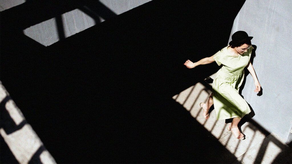 woman in black hat and green summer dress running up the stairs