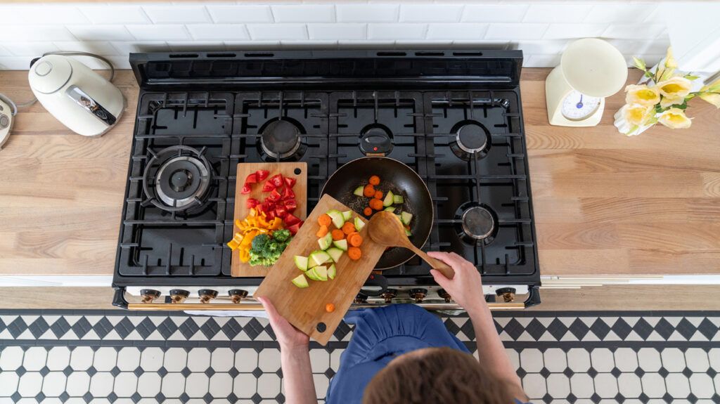 A woman preparing a healthy meal in the kitchen with a range of chopped vegetables, which are good for perimenopause diet. -1