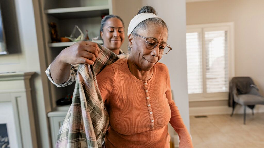 a caregiver helping an older woman put on her coat-1