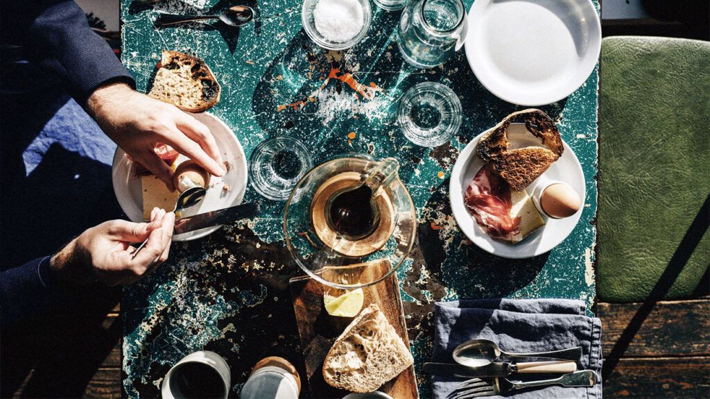 Aperson having breakfast with boiled eggs, sourdough bread, tea, and various other items early in the morning.