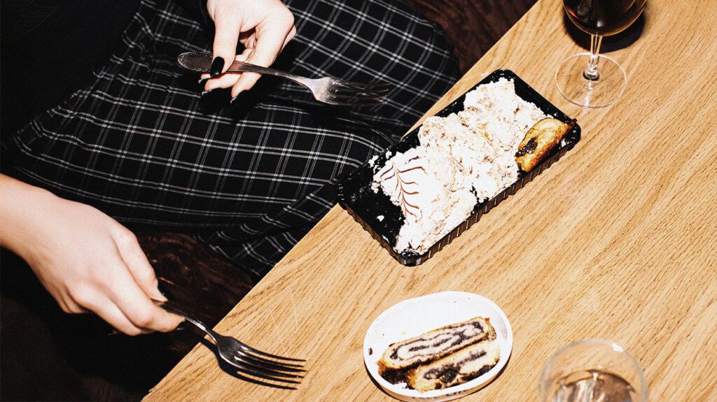 A person holding two forks and getting ready to eat a slice of marble cake and another dessert at a table