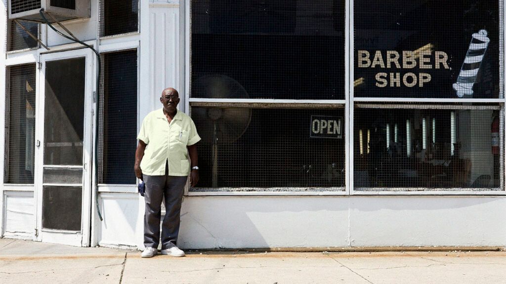 Older male standing in front of a barber shop window