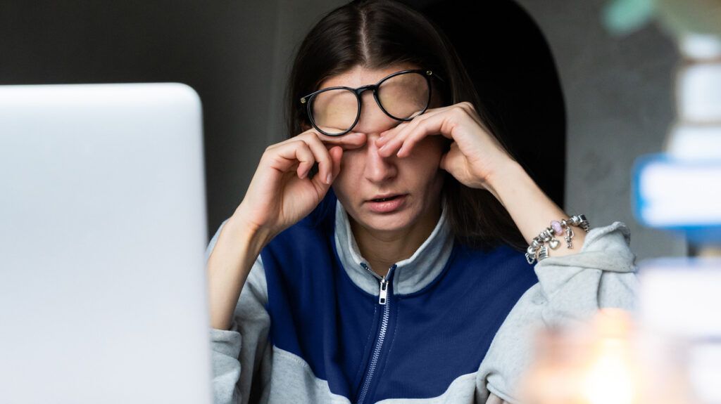 Fatigued woman rubbing her eyes, sat at a laptop