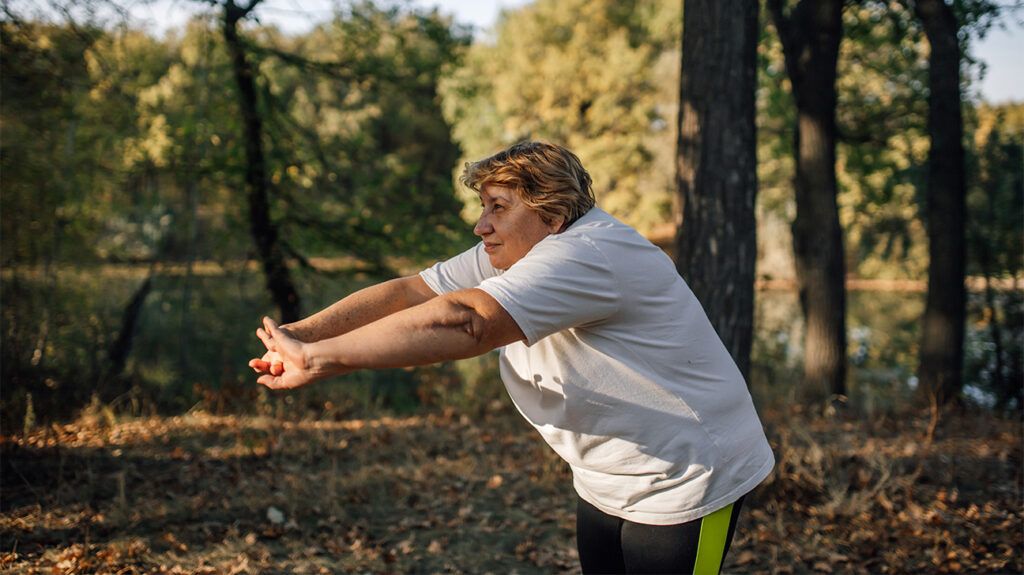 An older woman stretching outside in nature