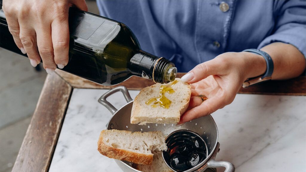 a person's hands pour olive oil on a slice of bread