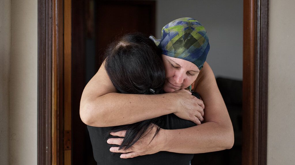 A person wearing a bandana after receiving chemotherapy treatment for cancer hugs another human