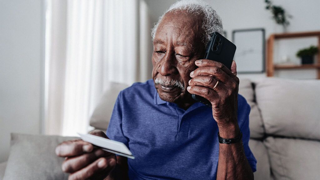 Older male holding a Medicare flex card and talking on the phone